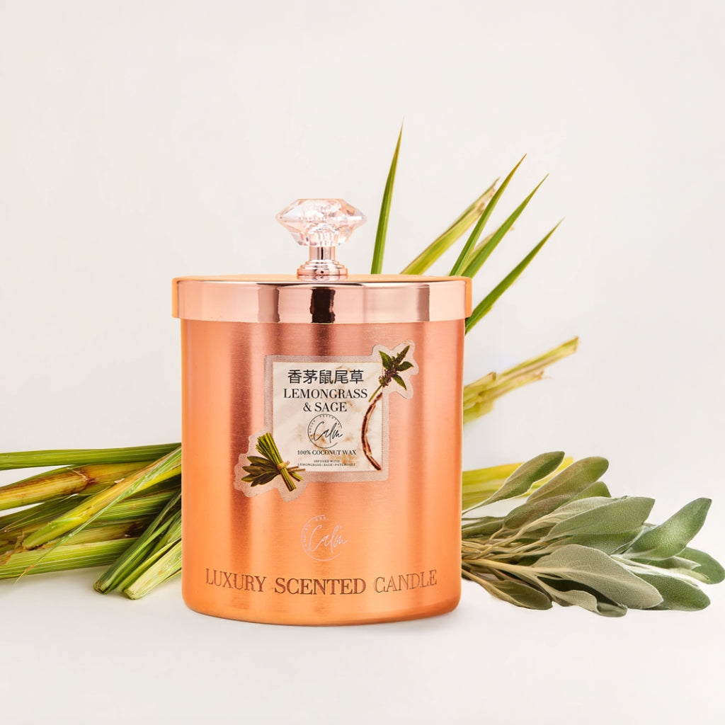 Luxury scented candle with rose gold container and decorative label on a light background with green leaves.